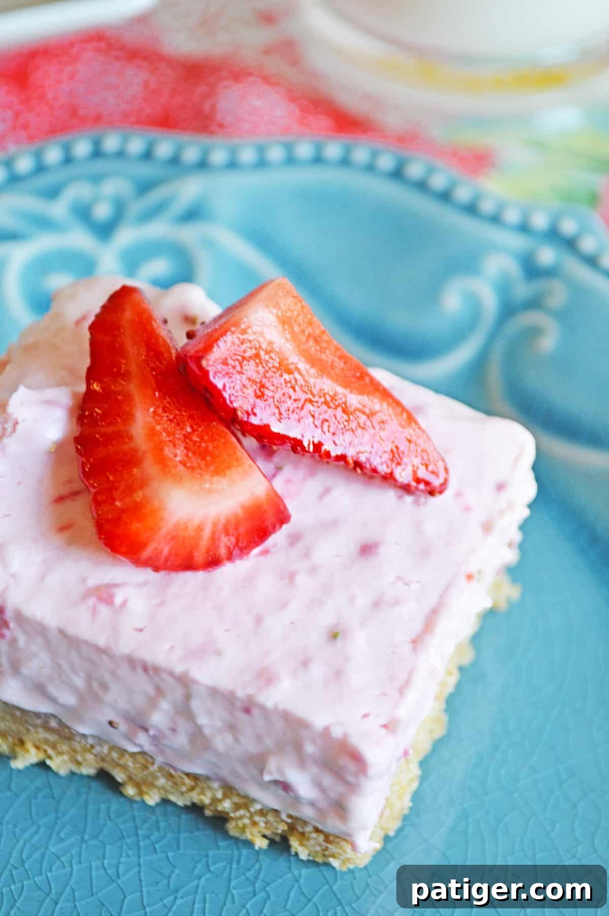 A close-up shot of a perfectly cut strawberry no-bake cheesecake bar, featuring a golden graham cracker crust and a smooth, pink filling topped with fresh strawberry slices, highlighting its delectable appearance.