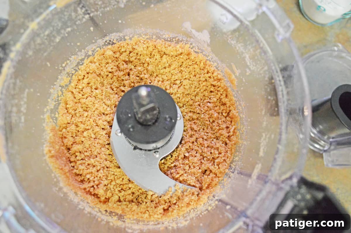 A food processor bowl filled with finely pulsed graham crackers, demonstrating the process of making fresh graham cracker crumbs for the crust.