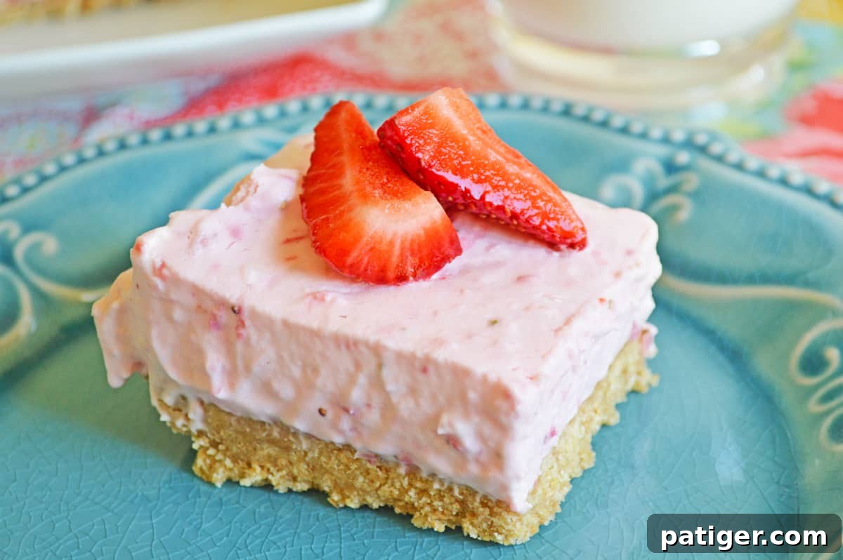 A perfectly portioned No-Bake Strawberry Cheesecake Bar, showcasing its thick graham cracker crust and smooth, creamy filling, topped with fresh strawberries, served on a vibrant blue plate.