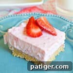 A small image of a No-Bake Strawberry Cheesecake Bar with a thick graham cracker crust and fresh strawberry toppings, on a blue plate.