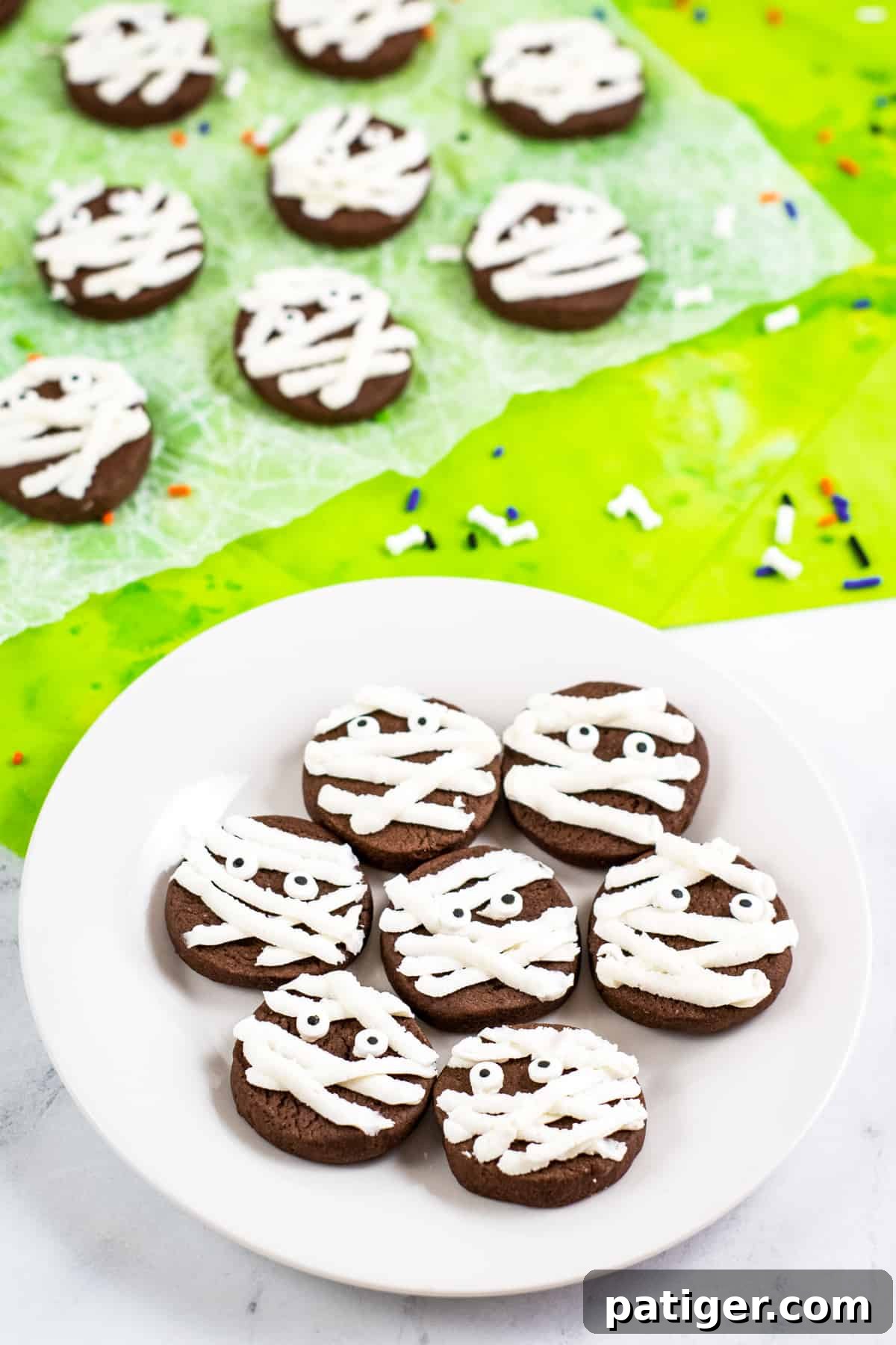Mummy cookies on white plate with additional mummy cookies on wax paper in background