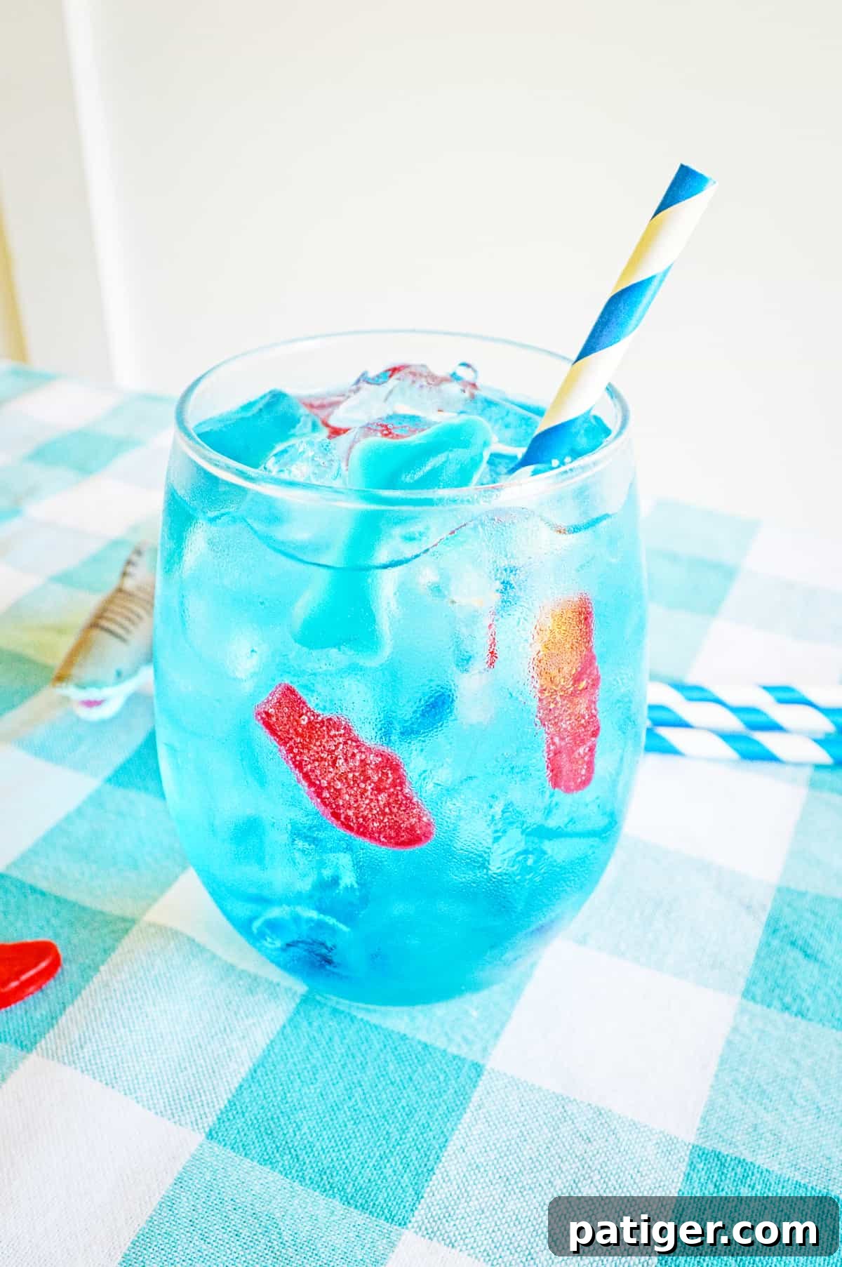 Blue ocean water drink in glass with ice, gummy fish, gummy shark, and blue and white paper straw