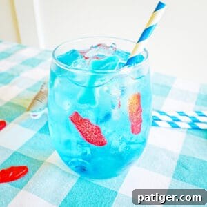 Blue ocean water drink in glass with ice, gummy fish, gummy shark, and blue and white paper straw