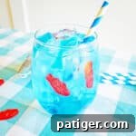 Blue ocean water drink in glass with ice, gummy fish, gummy shark, and blue and white paper straw
