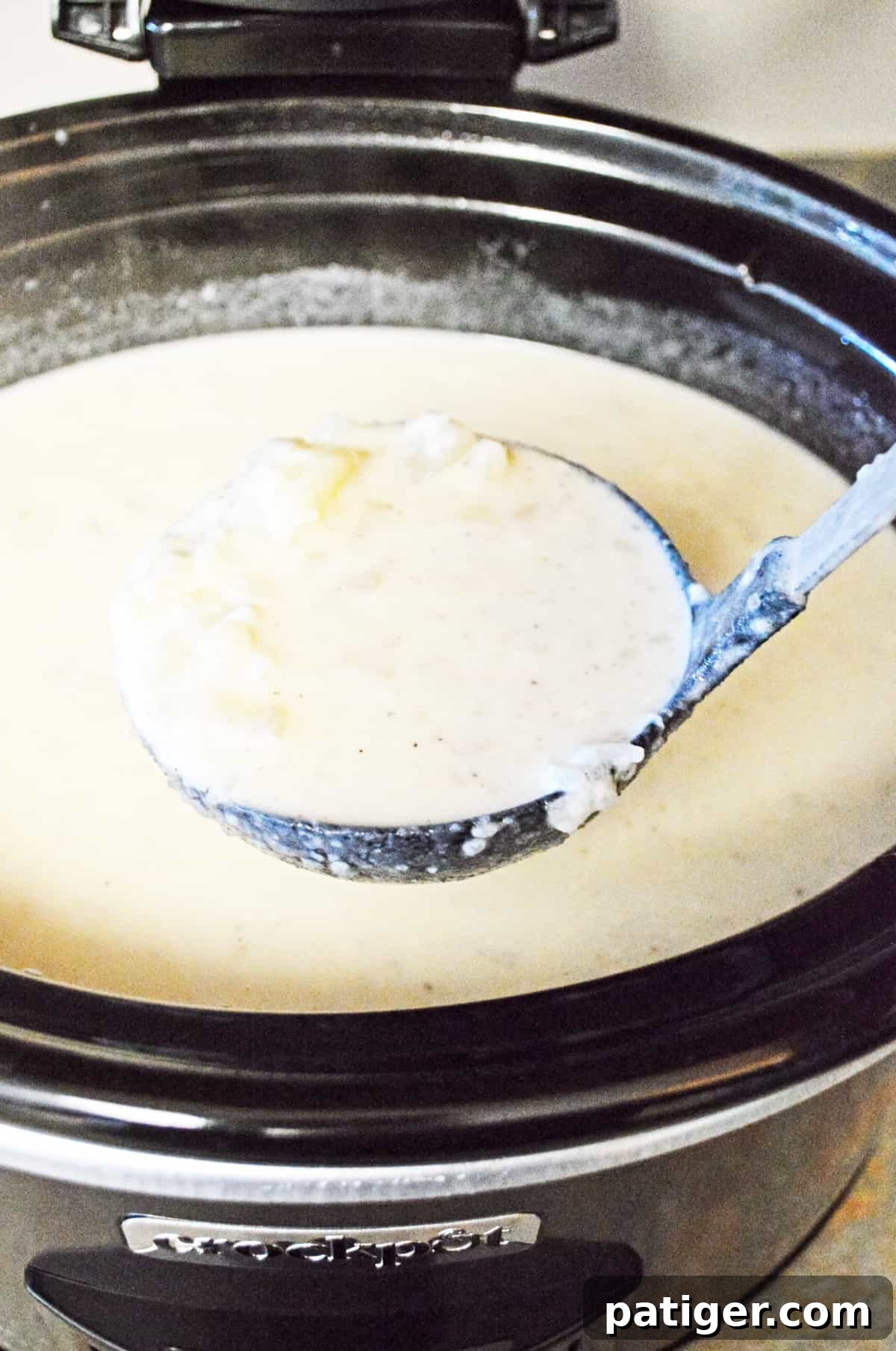 A close-up view of creamy baked potato soup simmering gently in a slow cooker, showcasing its rich, thick texture after the final ingredients have been incorporated.