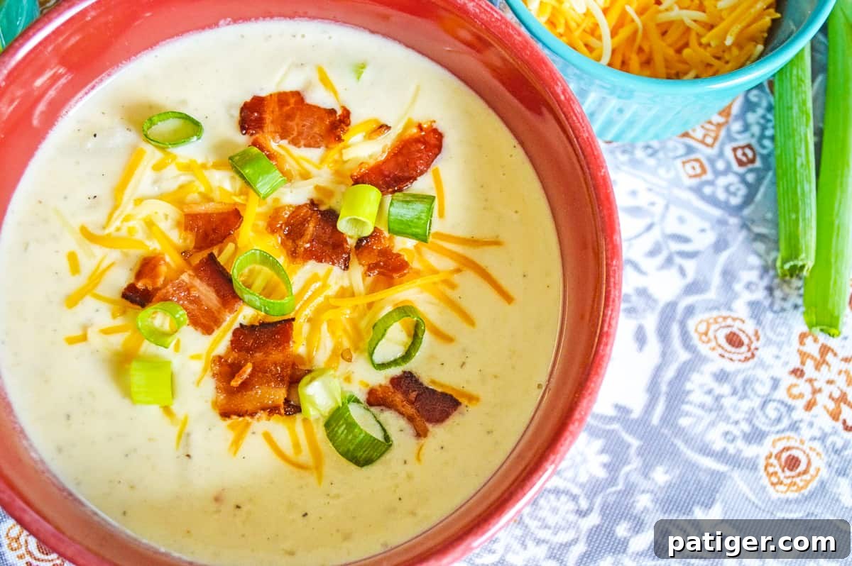 A top-down view of a steaming bowl of crockpot loaded baked potato soup, lavishly garnished with crispy bacon bits, vibrant green onions, and melted shredded cheese, ready to be enjoyed.