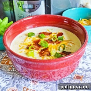 A vibrant red bowl filled with creamy crockpot loaded baked potato soup, generously topped with crispy bacon, fresh scallions, and melted cheese, ready to be enjoyed.