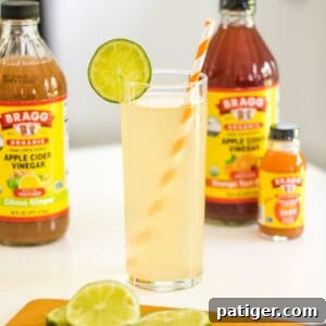 Apple cider vinegar mocktail with lime garnish and bragg apple cider vinegar in the background