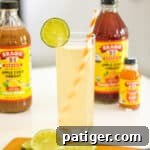 Apple cider vinegar mocktail with lime garnish and bragg apple cider vinegar in the background