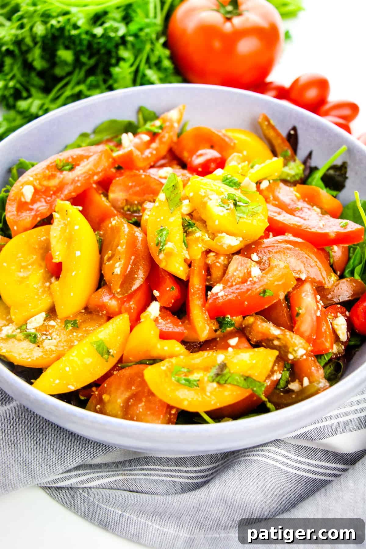 Vibrant Heirloom Tomato Salad served in a large grey bowl on a bed of fresh lettuce, garnished with parsley. Uncut tomatoes and additional parsley are visible in the background, highlighting the freshness of the ingredients.