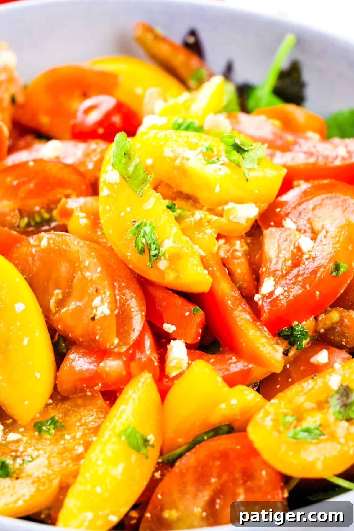 A close-up photograph of an Heirloom Tomato Salad, showcasing various colored tomato slices, crumbled feta cheese, and a glossy balsamic vinaigrette. The texture of the tomatoes and the vibrant colors are highlighted.