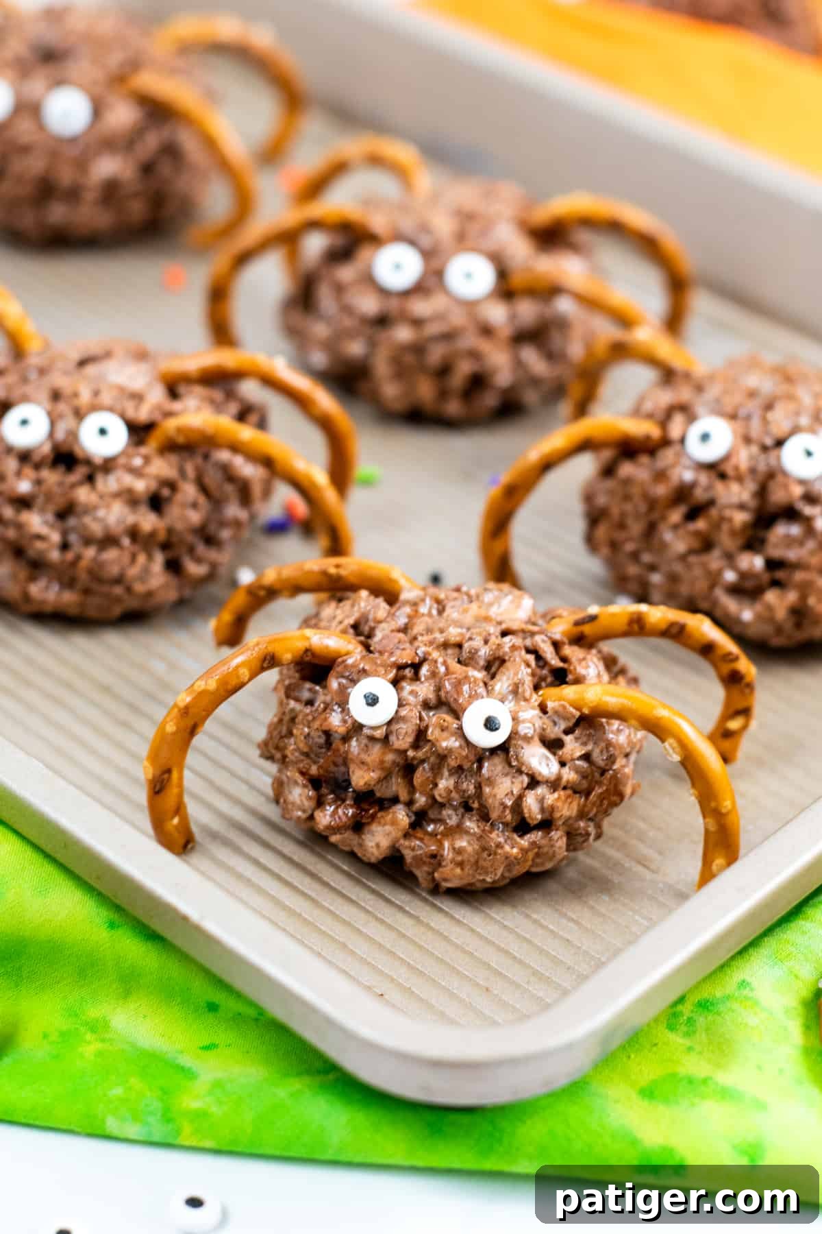 Close-up of round chocolate rice cereal treats with thin pretzel legs and bright candy eyes, ready for a Halloween party