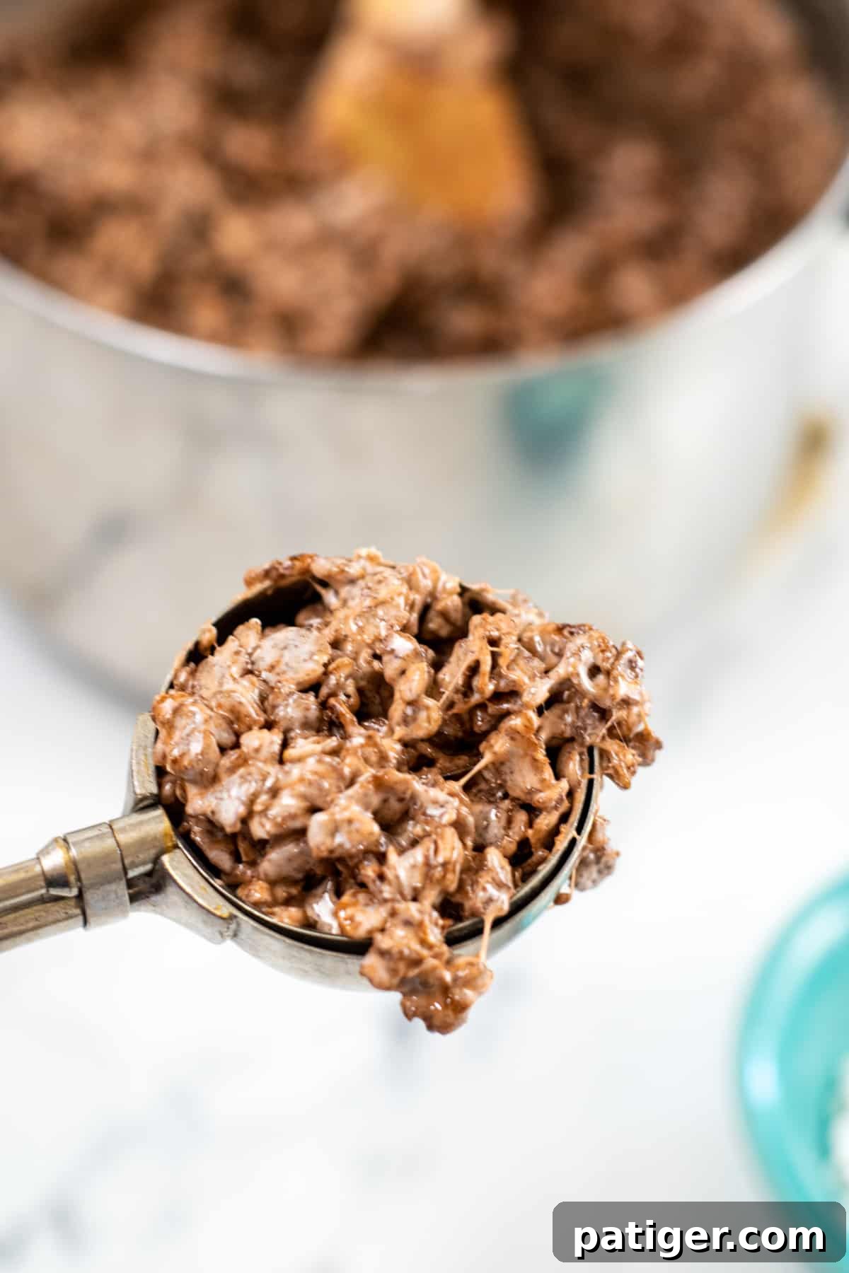 A scoop of rich cocoa krispie treat mixture, showcasing its sticky, ready-to-be-shaped texture.