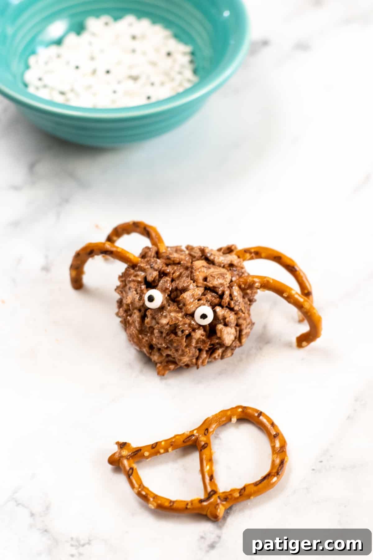 A perfectly decorated round rice cereal treat spider with four pretzel legs and two candy eyes, ready to be served for Halloween.