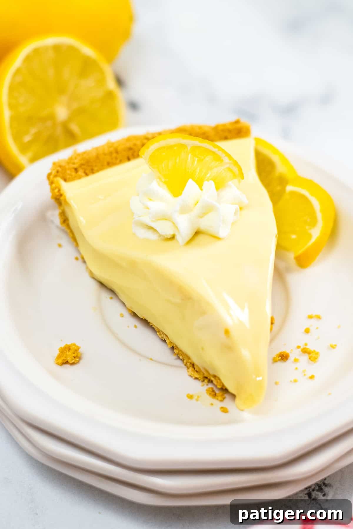 A tempting piece of no-bake lemon pie featuring a golden graham cracker crust, beautifully topped with a swirl of whipped cream and a delicate lemon slice, ready to be enjoyed.