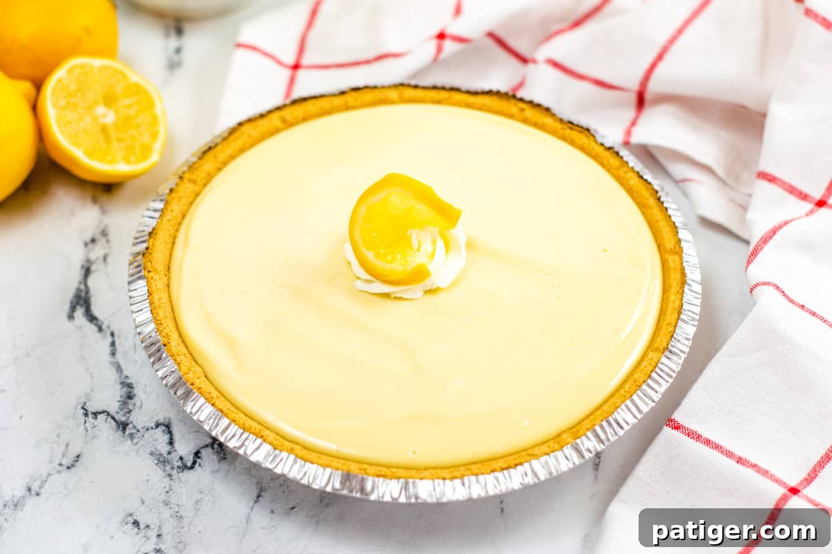 A freshly made lemon pie in a pre-made graham cracker crust, elegantly garnished in the center with a dollop of whipped cream and a slice of lemon.