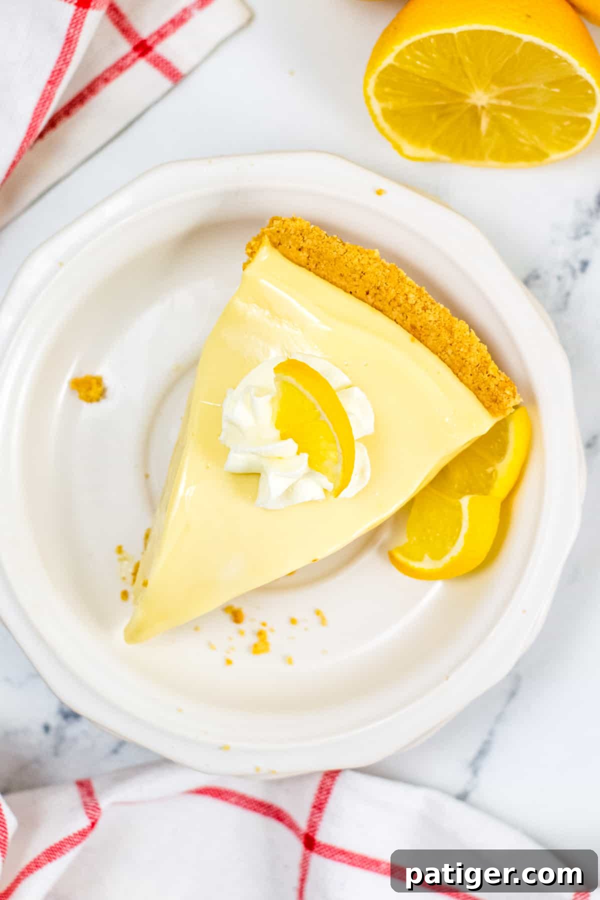 A close-up view of a slice of no-bake lemon pie, showcasing its smooth, creamy filling and distinct graham cracker crust, topped with a delicate dollop of whipped cream.