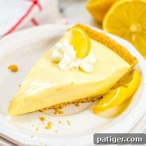 Lemon Icebox Pie slice on white plate, topped with whipped cream and lemon slice