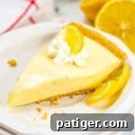 Lemon Icebox Pie slice on white plate, topped with whipped cream and lemon slice