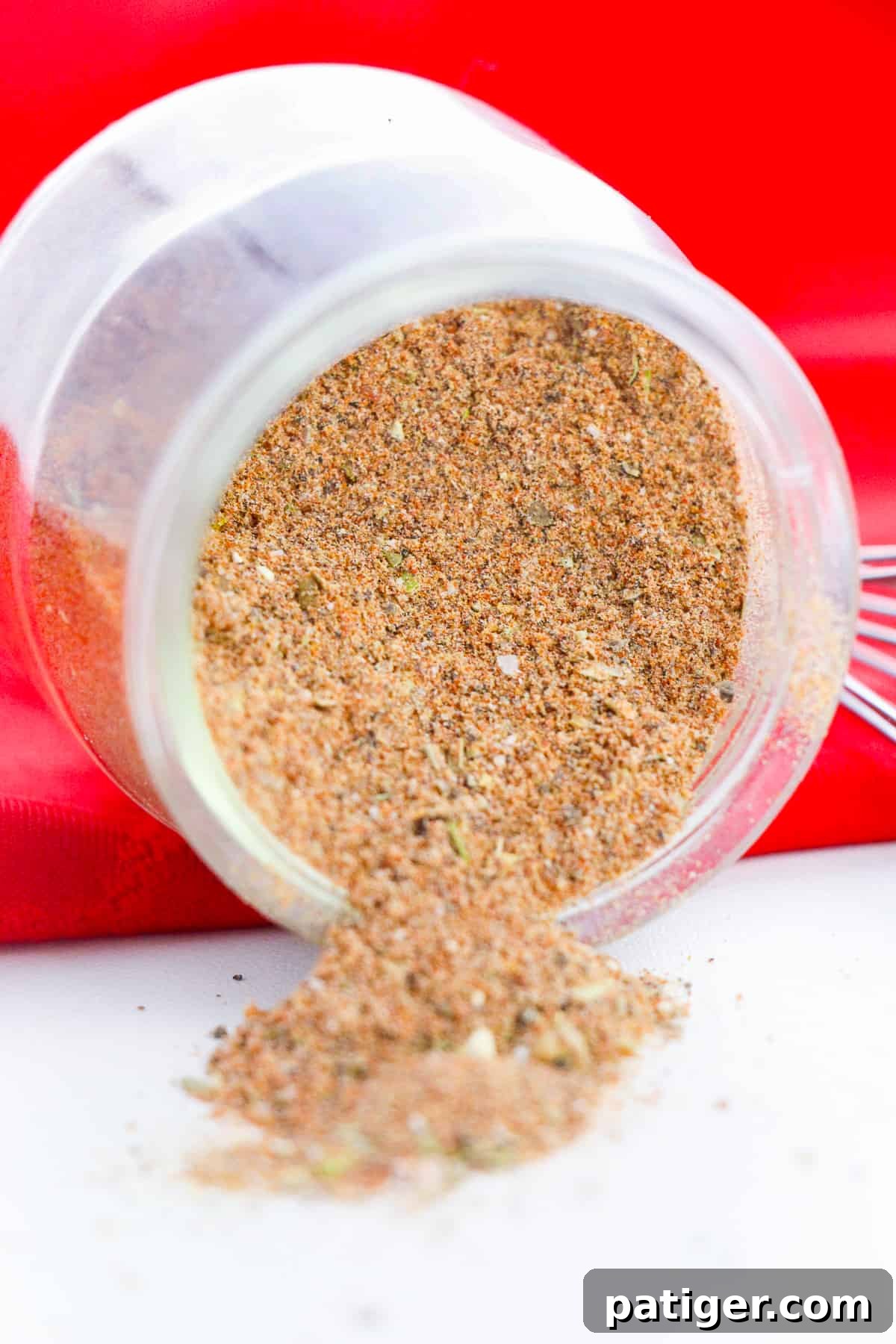 Craft Your Own Chili Spice Blend 3 Jar of homemade chili seasoning mix laying down on its side with the seasoning falling out onto tabletop, highlighting its fresh, vibrant texture.