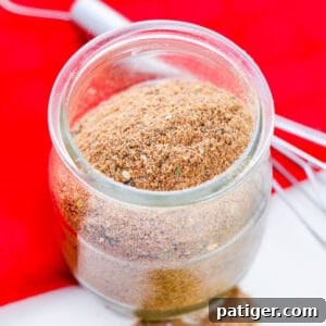 Homemade Chili Seasoning Mix in small glass jar with wire whisk next to it, a beautiful photo for the recipe card.