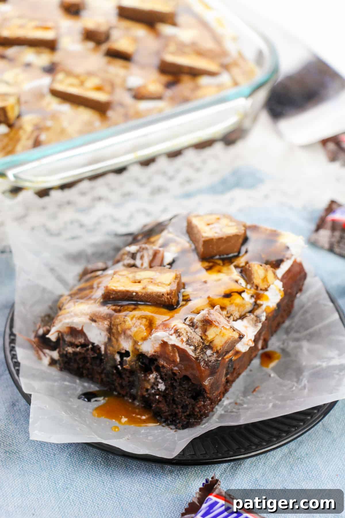 Snickers poke cake made with chocolate cake, chocolate pudding, caramel sauce, peanuts, cool whip, chocolate sauce, and chopped Snickers candy bars.