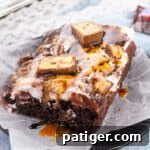 Snickers poke cake made with chocolate cake, chocolate pudding, caramel sauce, peanuts, cool whip, chocolate sauce, and chopped Snickers candy bars.