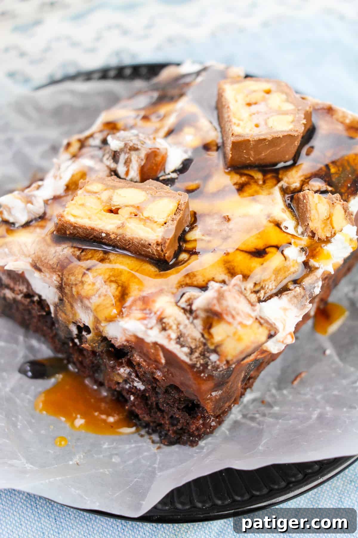 Snickers chocolate cake with whipped topping and chocolate and caramel sauces drizzled on top, garnished with Snickers pieces.
