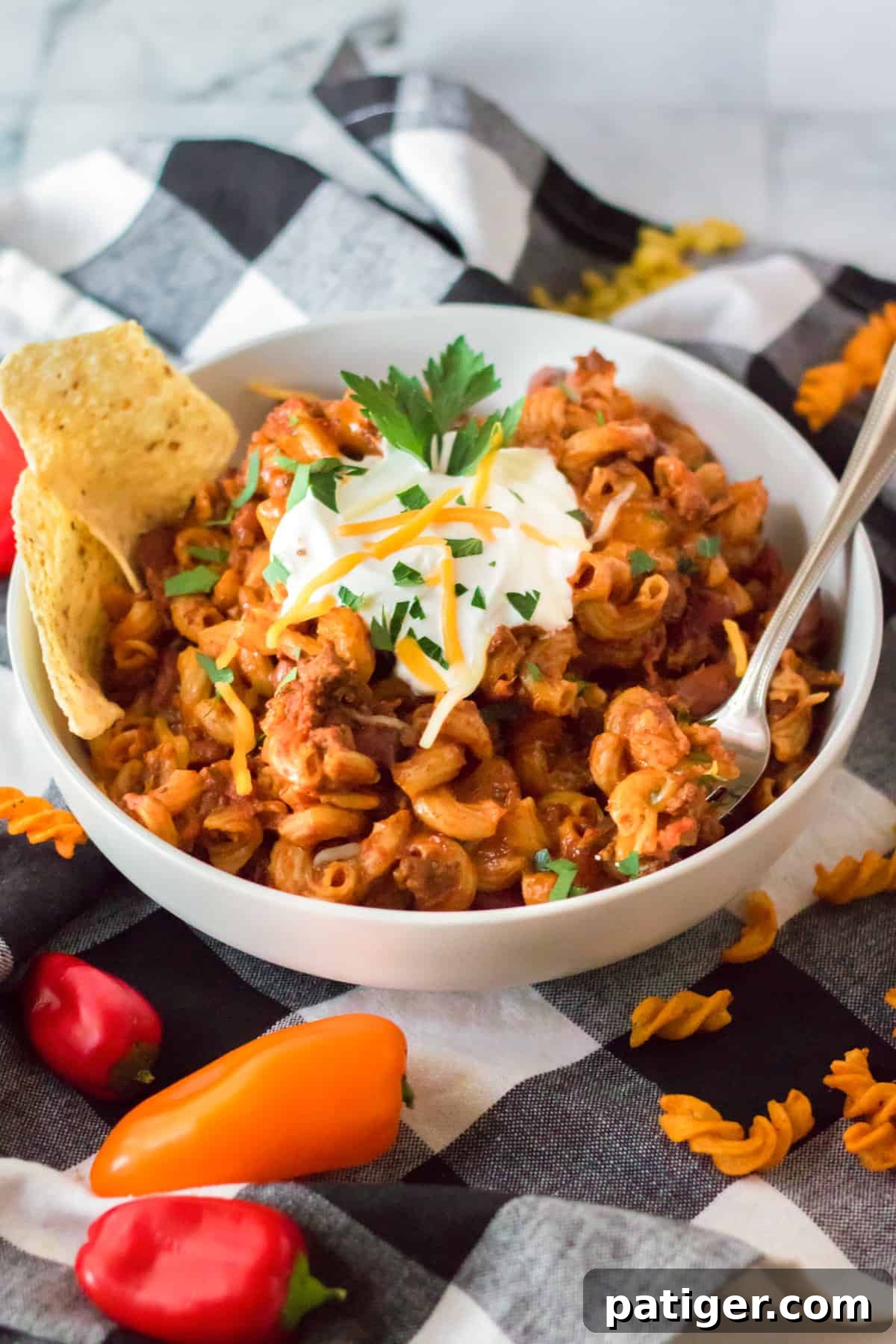 A steaming bowl of slow cooker chili mac, garnished with a dollop of sour cream, shredded cheese, fresh parsley, and crunchy tortilla chips.