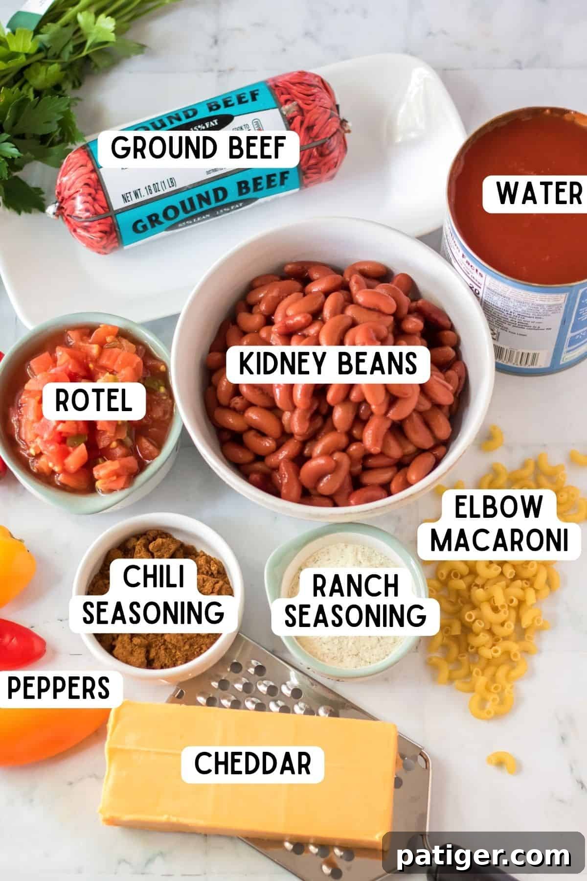 Array of ingredients for Chili Mac including kidney beans, ground beef, Rotel, chili seasoning, ranch seasoning, elbow macaroni, bell peppers, water, and a block of cheddar cheese.