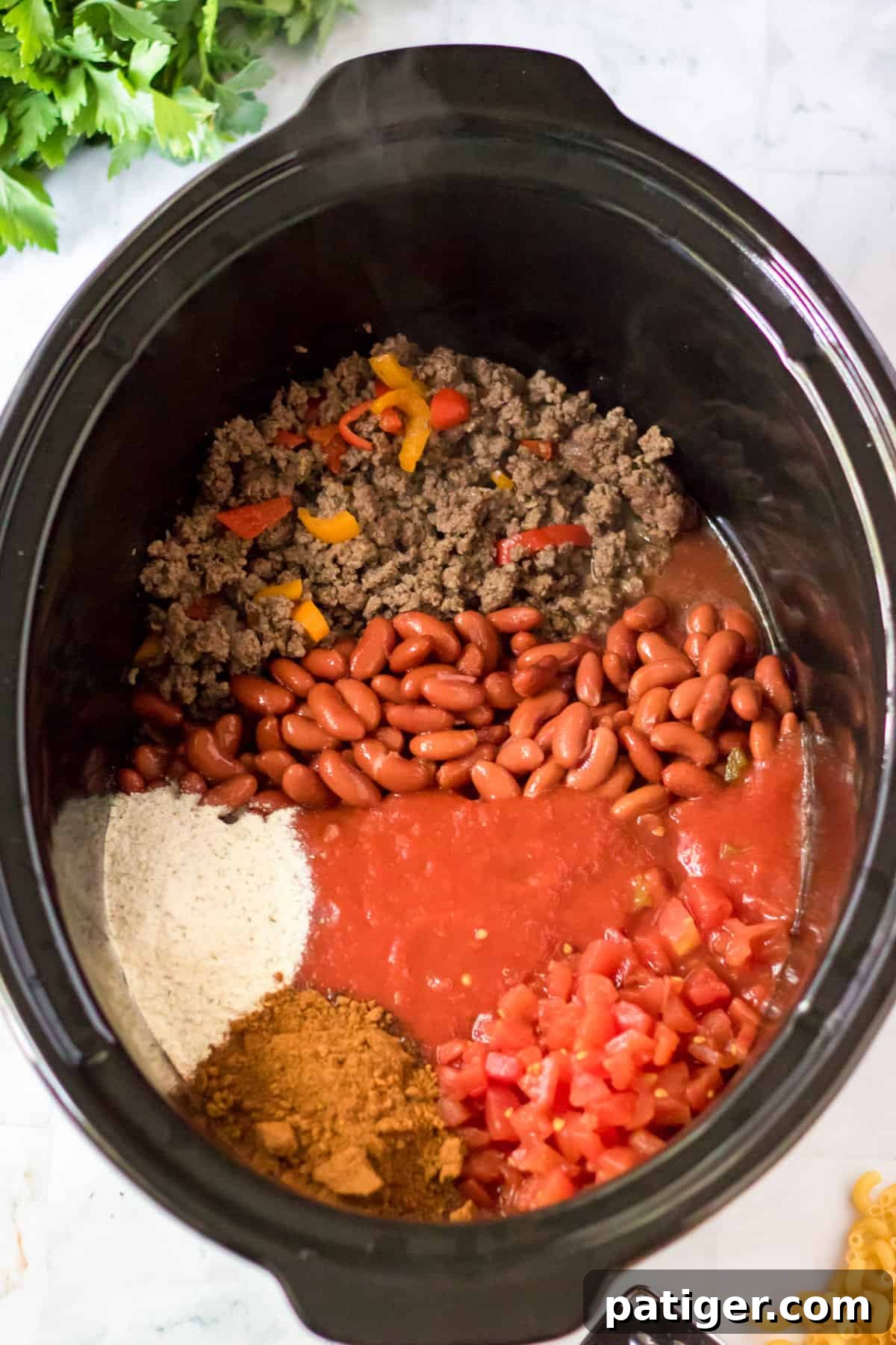 Ground beef, peppers, beans, Rotel tomatoes, water, tomato sauce, and various seasonings loaded into a slow cooker.