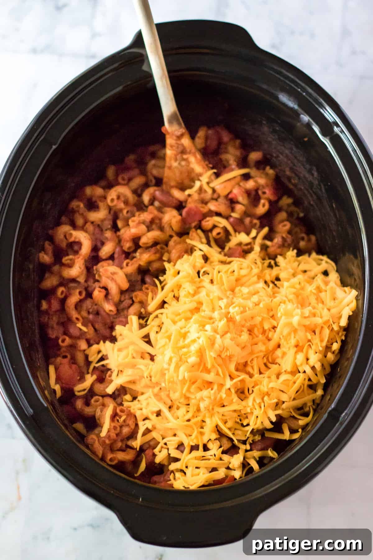 Shredded cheddar cheese being added and stirred into the slow cooker chili mac.