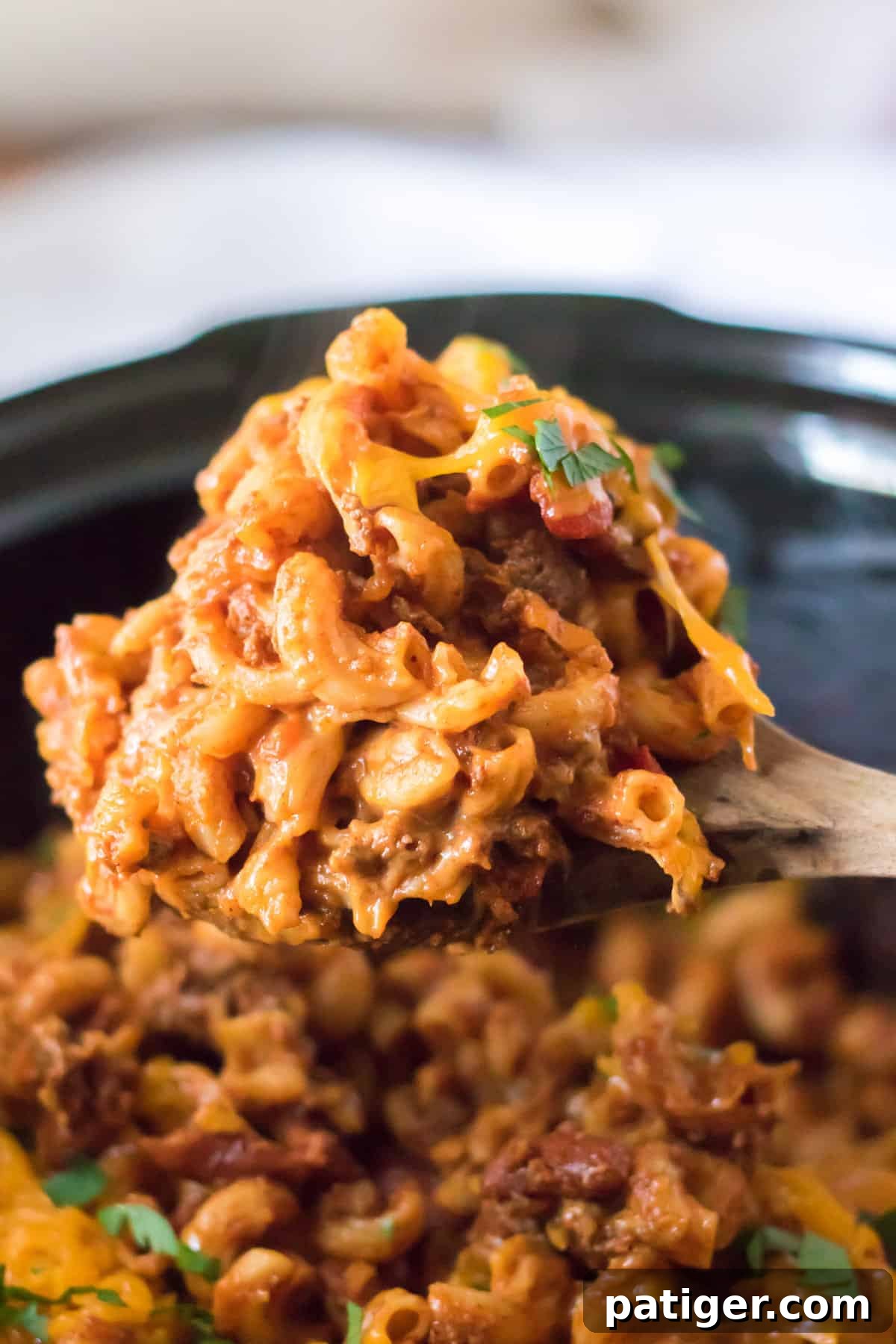 Slow cooker chili mac with beans and ground beef being scooped from a bowl, highlighting its hearty texture.