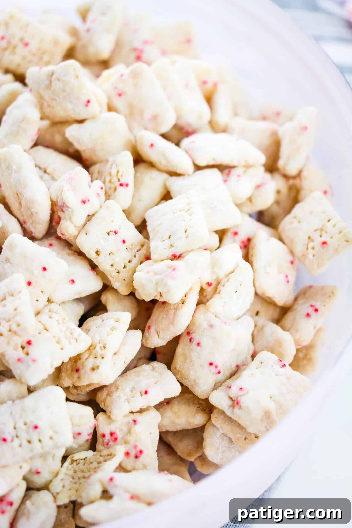 Winter Mint Bark Buddy Bites 2 A white bowl filled with festive Peppermint Bark Muddy Buddies, a perfect holiday snack.