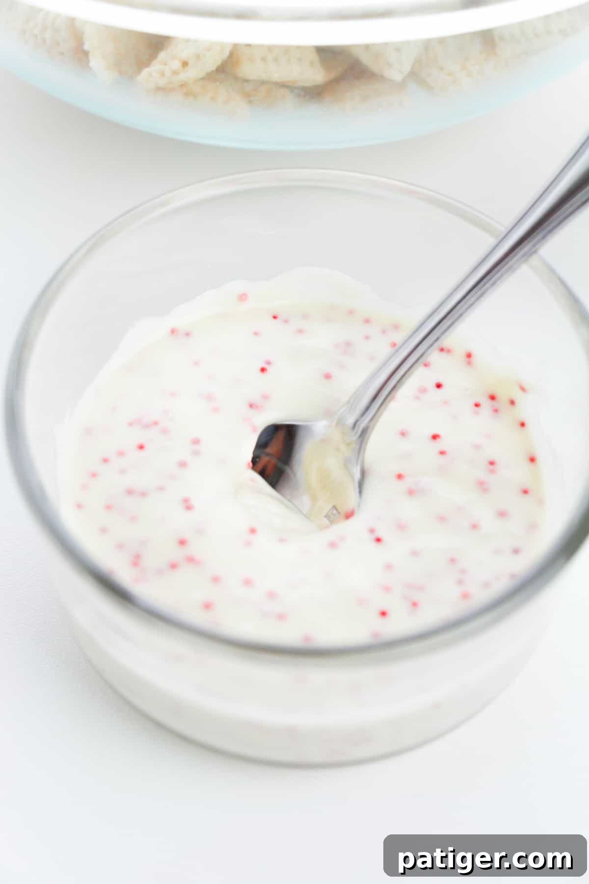 Winter Mint Bark Buddy Bites 6 A glass bowl with perfectly melted white chocolate infused with red peppermint specks, ready to coat the cereal.