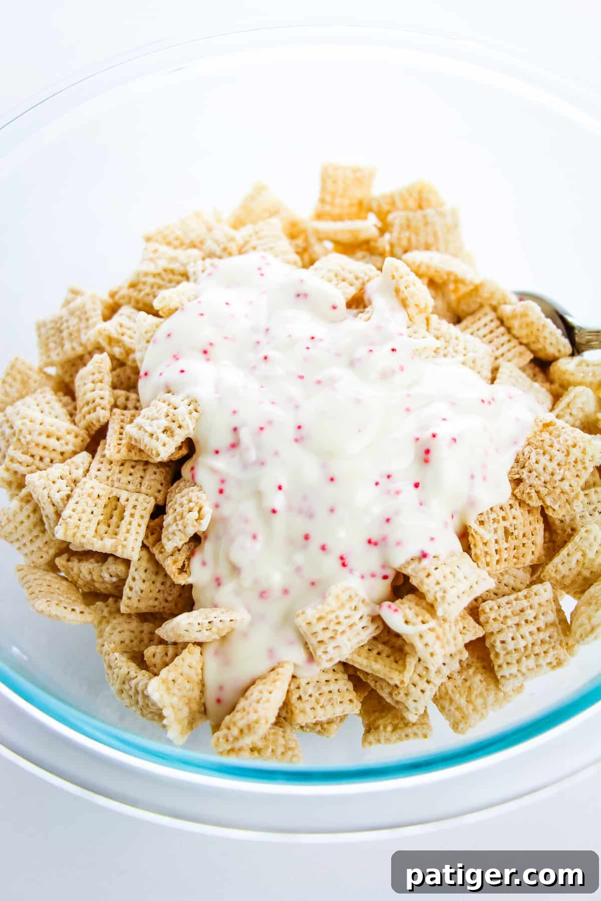 Winter Mint Bark Buddy Bites 7 Melted peppermint bark being poured over the dry Chex cereal in a large glass bowl.