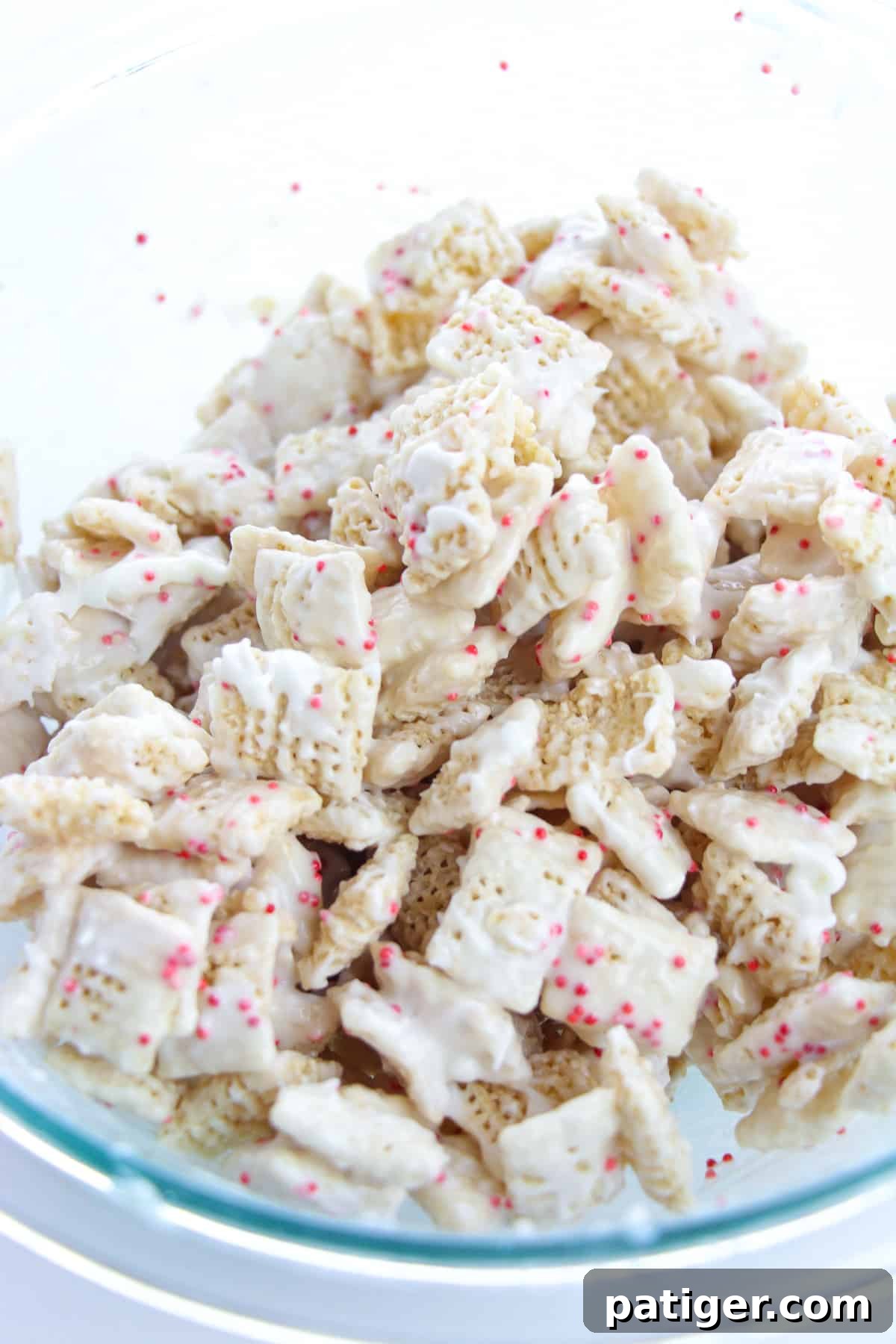 Winter Mint Bark Buddy Bites 8 Peppermint bark coated Chex cereal gently stirred in a large glass bowl, showing the even coverage.