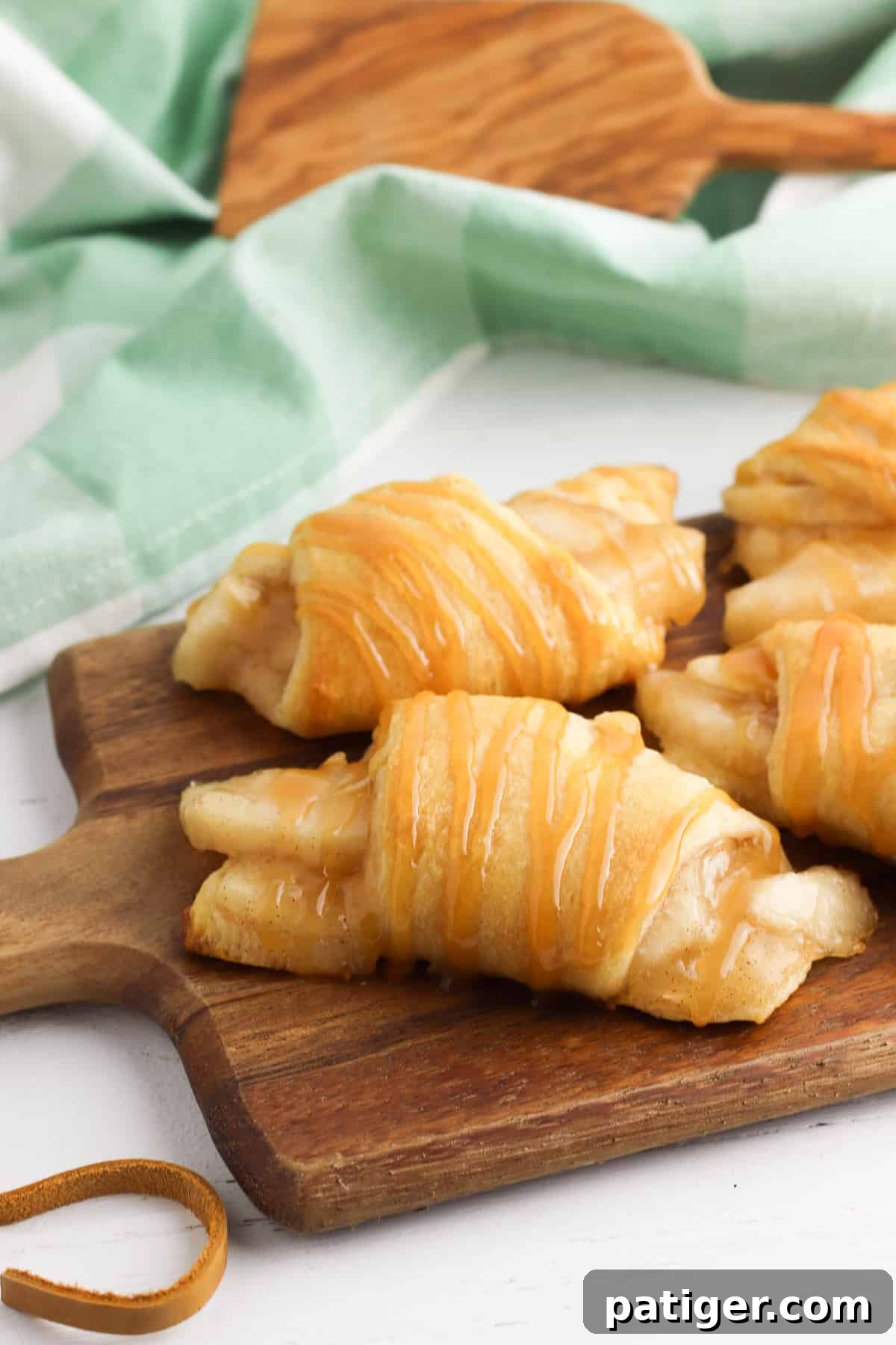 Crescent rolls filled with apple pie filling and drizzles with caramel sauce on wooden cutting board
