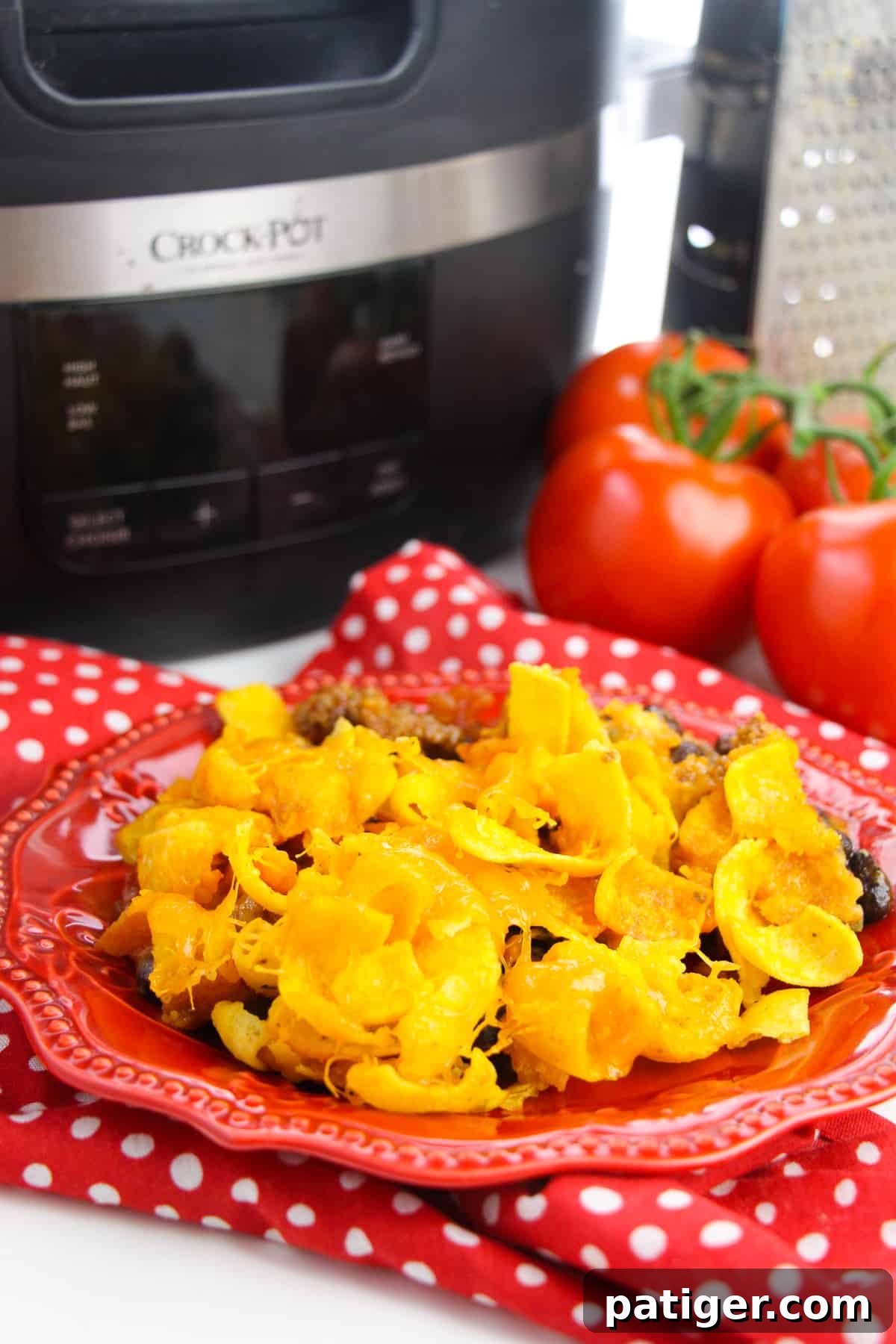 Slow Cooker Cheesy Frito Chili Bake 2 Delicious Crockpot Frito Pie served on a red plate, with a slow cooker and fresh ingredients in the background