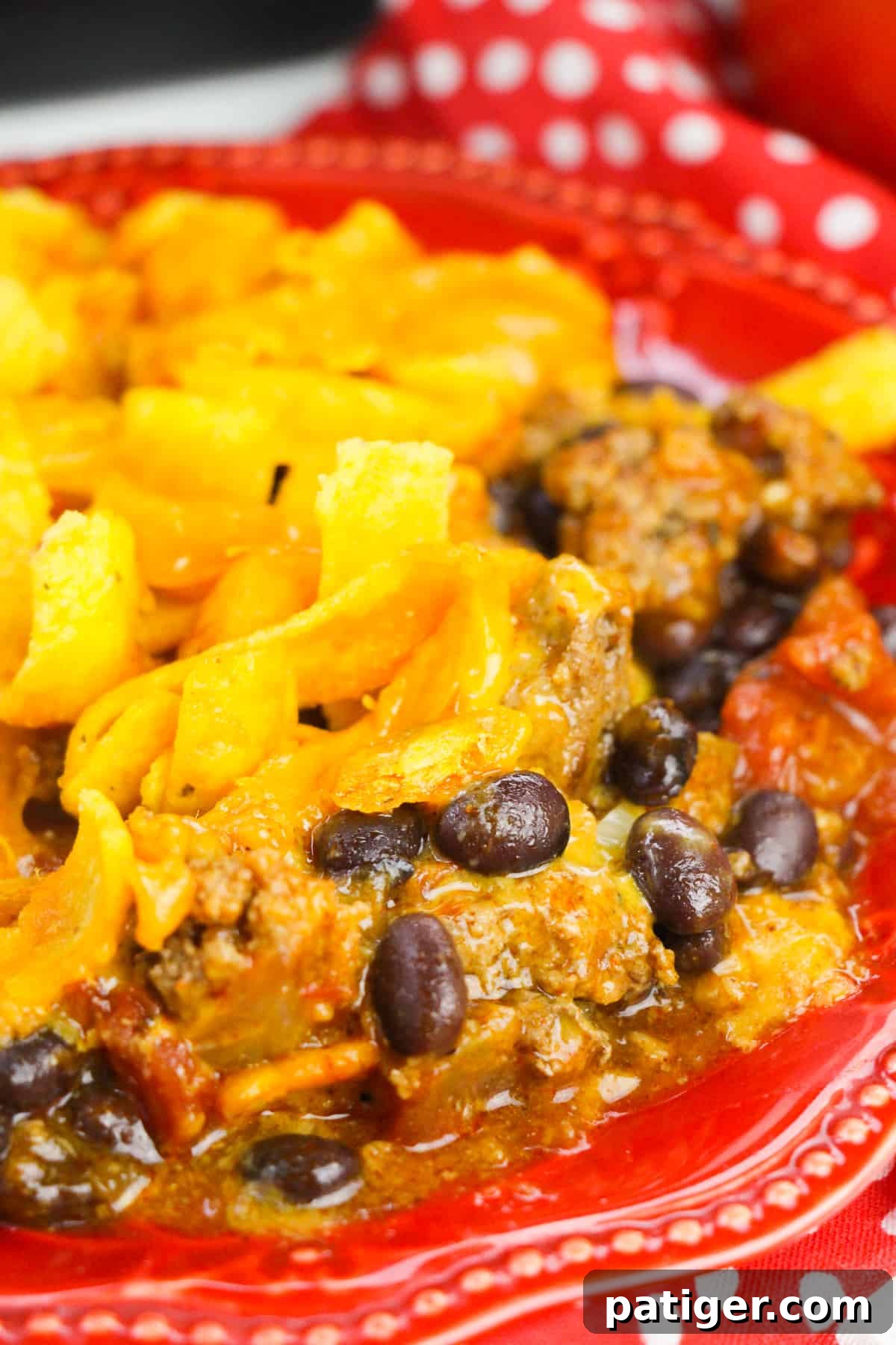 Slow Cooker Cheesy Frito Chili Bake 3 An individual serving of Frito pie on a vibrant red plate, garnished with fresh herbs