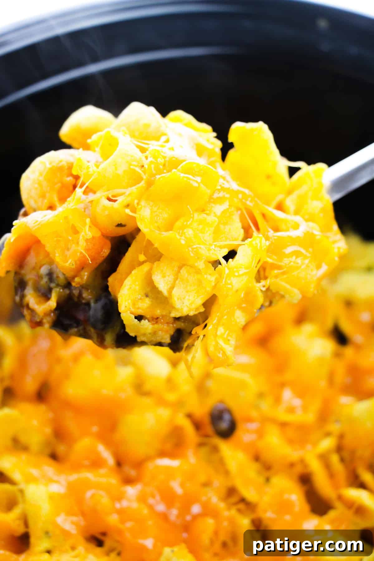 Slow Cooker Cheesy Frito Chili Bake 5 A large serving spoon scooping a portion of Frito Casserole from the crockpot, showing delicious layers of beef, beans, melted cheese, and Fritos