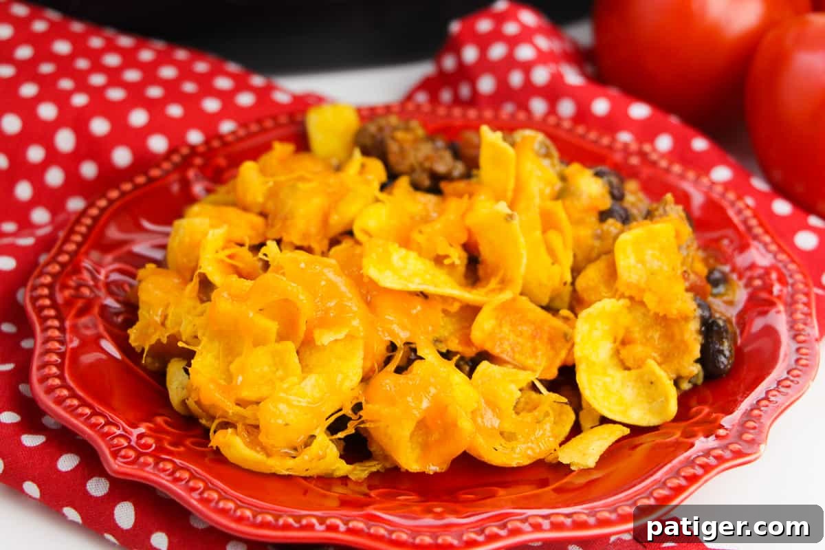 Slow Cooker Cheesy Frito Chili Bake 6 Close-up view of Crockpot Frito Casserole served on a red plate, with a red napkin and fresh tomatoes in the background