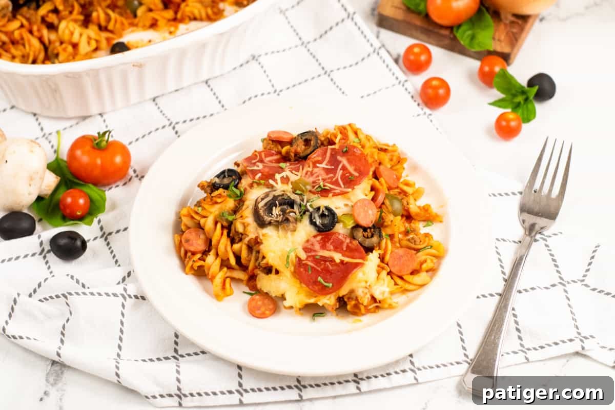 Serving of Cheesy Pizza Pasta Casserole on a white plate with the full dish in background