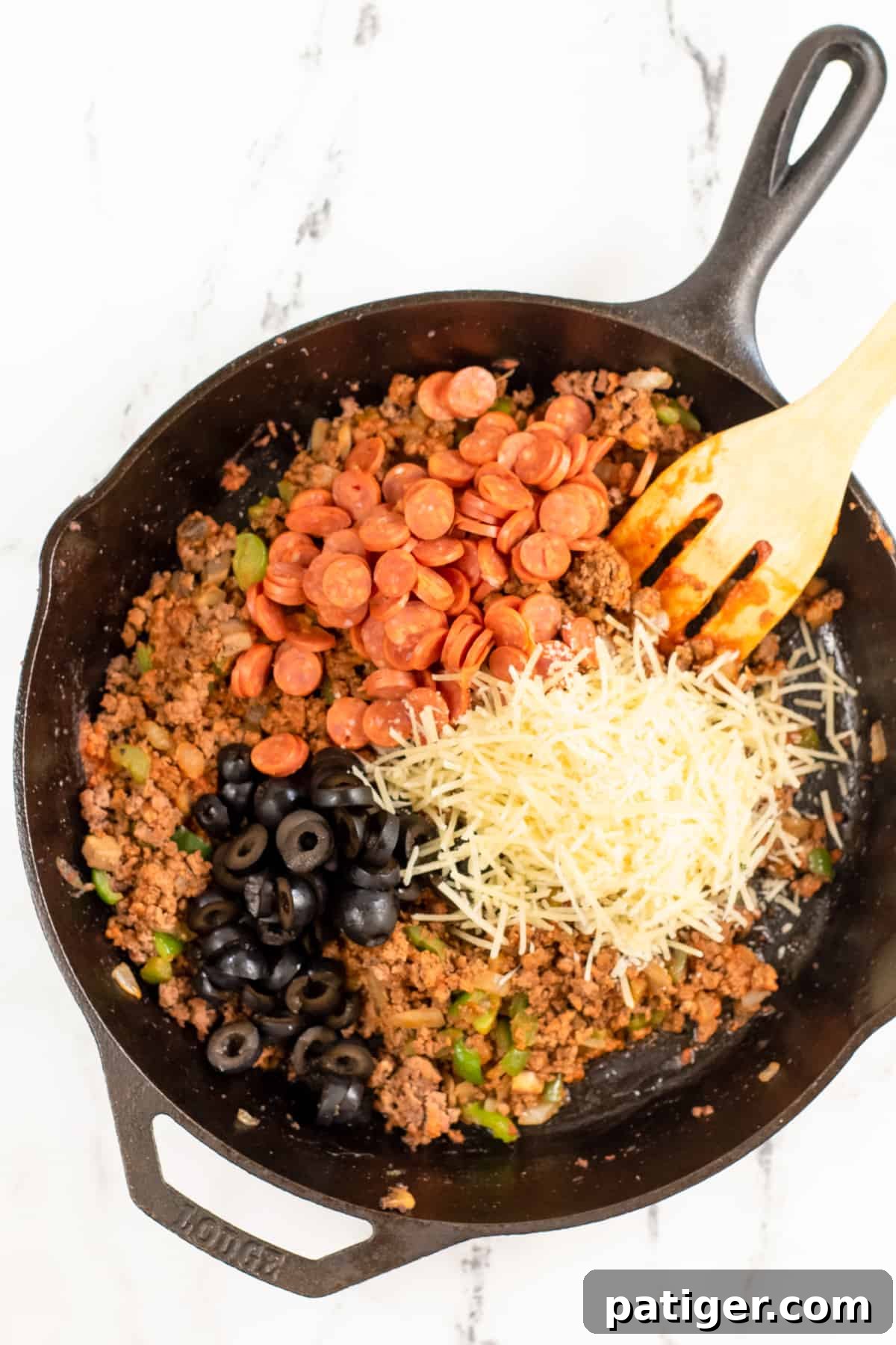 Ground beef mixture with mini pepperoni, shredded parmesan cheese, and black olives in a skillet