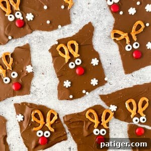 Chocolate reindeer bark broken into irregularly shaped pieces, each decorated with broken pretzels, candy eyes, and a red M&M to look like Rudolph the red-nosed reindeer