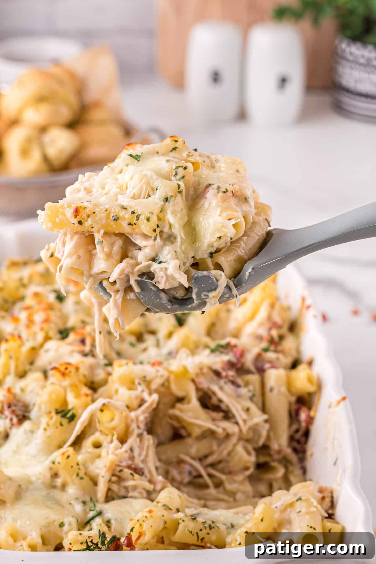 Golden Alfredo Chicken Bake 2 Large grey serving spoon scooping up a generous portion of creamy chicken alfredo casserole with bacon, cheese, and fresh parsley garnish.