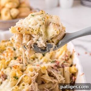 Large grey serving spoon scooping up a large serving of creamy chicken alfredo casserole with bacon, cheese, and parsley