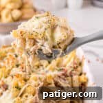 Large grey serving spoon scooping up a large serving of creamy chicken alfredo casserole with bacon, cheese, and parsley