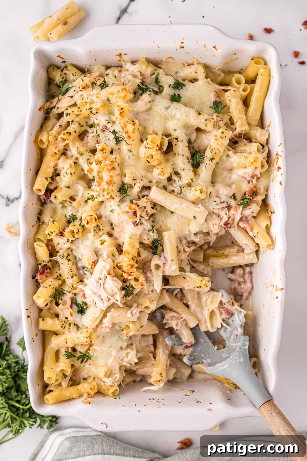Golden Alfredo Chicken Bake 3 Chicken Bacon Alfredo Pasta Bake in a 9x13 casserole dish with a portion scooped out, showcasing the creamy texture and ingredients.