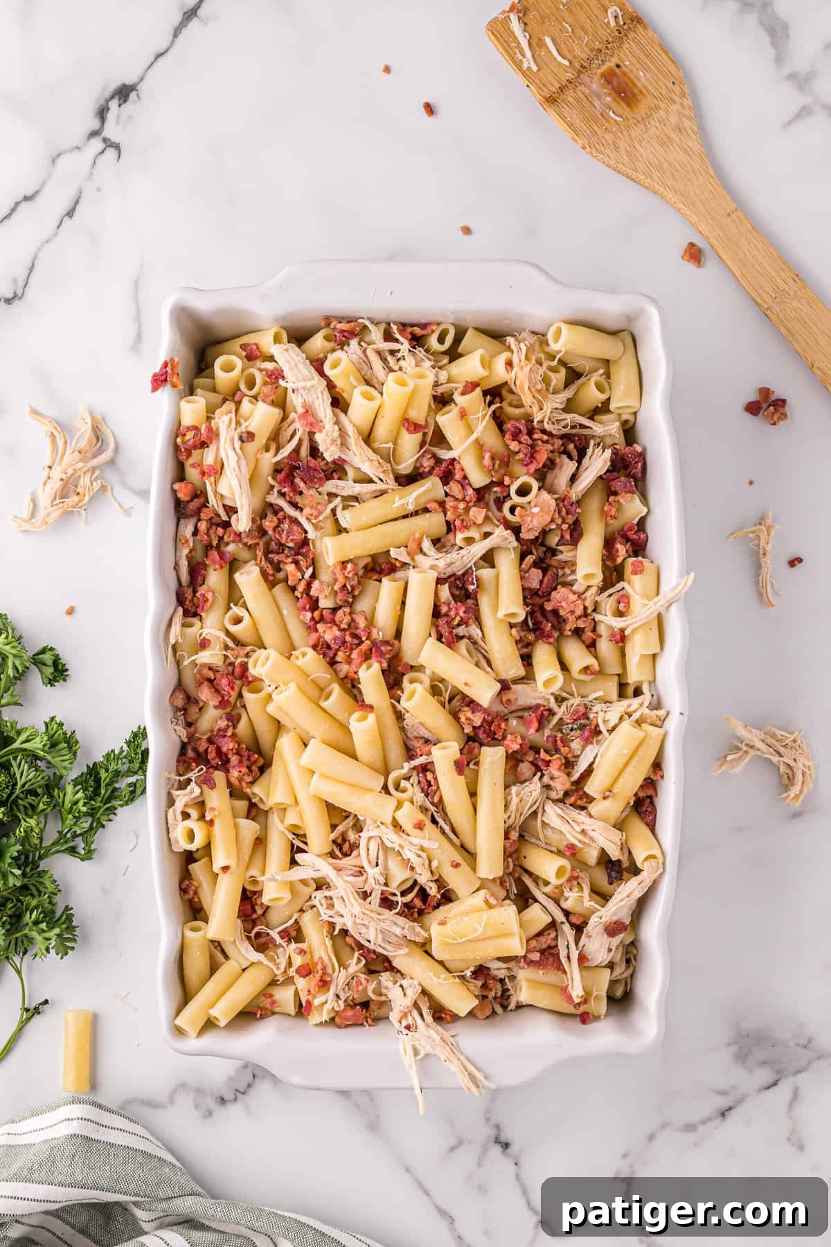 Golden Alfredo Chicken Bake 7 Casserole dish filled with cooked ziti, crumbled bacon, and shredded cooked chicken, ready for the sauce.